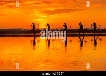 Frau Arbeiter die Körbe der frisch geerntete Salz auf ihren Schultern in Hon Khoi Salz Feld bei Sonnenaufgang, Nha Trang Provinz, Vietnam Stockfoto