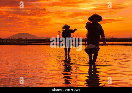 Frau Arbeiter die Körbe der frisch geerntete Salz auf ihren Schultern in Hon Khoi Salz Feld bei Sonnenaufgang, Nha Trang Provinz, Vietnam Stockfoto