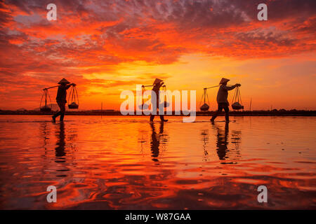 Frau Arbeiter die Körbe der frisch geerntete Salz auf ihren Schultern in Hon Khoi Salz Feld bei Sonnenaufgang, Nha Trang Provinz, Vietnam Stockfoto