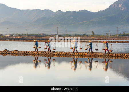 Frau Arbeiter die Körbe der frisch geerntete Salz auf ihren Schultern in Hon Khoi Salz Feld bei Sonnenaufgang, Nha Trang Provinz, Vietnam Stockfoto