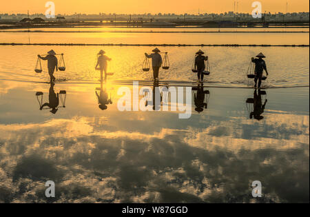 Frau Arbeiter die Körbe der frisch geerntete Salz auf ihren Schultern in Hon Khoi Salz Feld bei Sonnenaufgang, Nha Trang Provinz, Vietnam Stockfoto