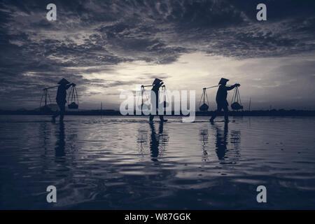 Frau Arbeiter die Körbe der frisch geerntete Salz auf ihren Schultern in Hon Khoi Salz Feld bei Sonnenaufgang, Nha Trang Provinz, Vietnam Stockfoto