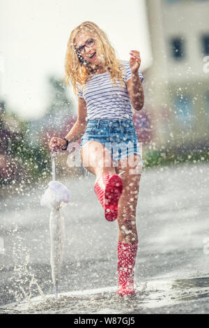 Fröhliches Mädchen springen mit weißer Schirm in punktierten roten Galoschen. Heißer Sommer Tag nach dem regen Frau springen und Plantschen in der Pfütze Stockfoto