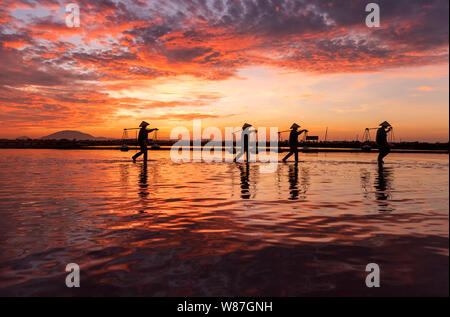 Frau Arbeiter die Körbe der frisch geerntete Salz auf ihren Schultern in Hon Khoi Salz Feld bei Sonnenaufgang, Nha Trang Provinz, Vietnam Stockfoto