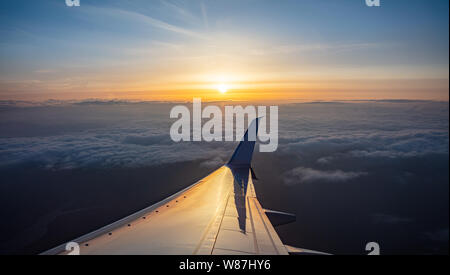 Sonnenuntergang Luftaufnahme aus einem Flugzeug Fenster. Sun fallen, Flugzeug fliegen über den Wolken. Farbe orange Sonnenstrahlen und Reflexionen auf der Ebene Flügel Stockfoto