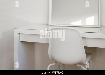 Breite Aufnahme eines Spiegels auf einem weißen Tisch mit Ein Stuhl vorne Stockfoto