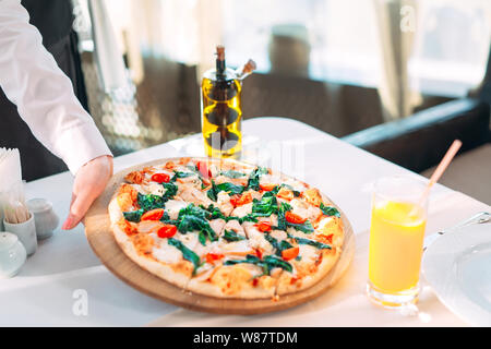 Stellt der Ober Pizza auf dem Tisch im Restaurant. Stockfoto
