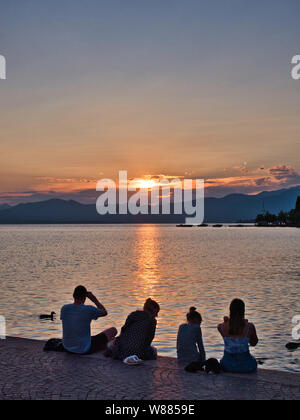 Eine Familie geniesst die schönen und warmen Sonnenuntergang über dem Gardasee sitzen am Ufer des Promenade, dass die Grenzen der See in der Ortschaft Bardolino Stockfoto