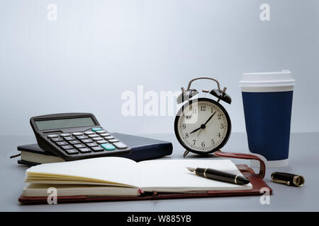 Wecker mit Notebook, Taschenrechner, Stift und Tasse Kaffee auf grauem Hintergrund auf die Tabelle Stockfoto