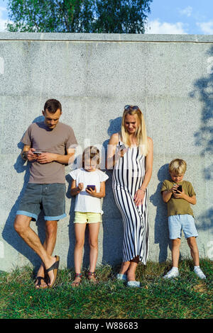 Bild des blonden Frau und Mann und Kinder mit Handys in den Händen stehend auf Betonwand auf der Straße Stockfoto