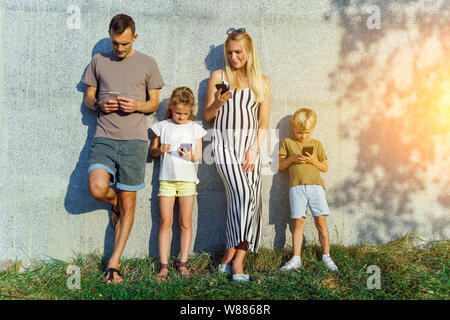 Bild von Eltern und Kindern mit Handys in den Händen stehend auf Betonwand auf der Straße Stockfoto