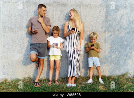 Foto von Eltern und Kindern mit Telefonen in der Hand stehen auf Betonwand auf der Straße Stockfoto