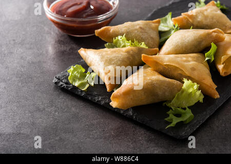 Samsa oder Samosas mit Fleisch und Gemüse auf schwarzem Hintergrund. Traditionelle indische Küche. Stockfoto