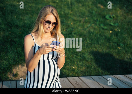 Foto der schwangeren Frau in langen Kleid mit dem Telefon in der Hand in der Nähe von See Stockfoto