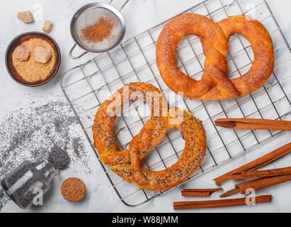 Brezel. Frisch gebackene Brezeln mit Zucker, Mohn und Zimt. Leckere hausgemachte Kuchen und Zutaten auf den Tisch. Selektiver Fokus, Ansicht von oben Stockfoto