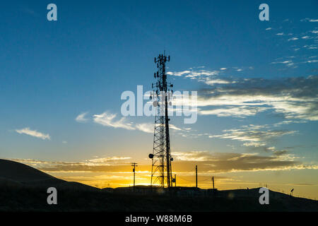 Ein Handy Kommunikation Turm, der von der untergehenden Sonne in der kalifornischen Central Valley entlang der Autobahn 5 USA Silhouette Stockfoto