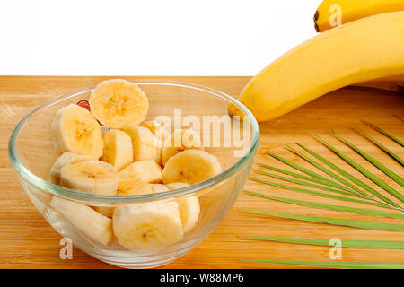 Bananenscheiben liegt in der Platte. Platte, Farn Bush, Bananen liegen auf einem Holzbrett. Weißer Hintergrund, isolieren. Stockfoto
