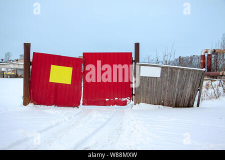 Alte Tor mit einem zerstörten Holzzaun in einem verlassenen Unternehmen. Zwei Vorlagen für Inschriften. Stockfoto