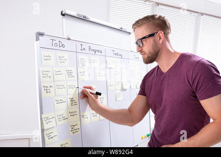 Seitenansicht der junge Geschäftsmann Schreiben auf Haftnotizen zu White Board In Office angeschlossen Stockfoto