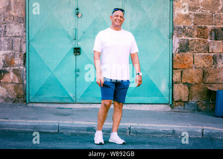 Senior touristische athletische im Nahen und Mittleren Osten Mann auf der Straße, genießen Sie einen wunderschönen Blick auf die Altstadt. Reisen, Freiheit, aktiven Lebensstil Konzept. Business lächelnd reifer Mann in Shorts und T-Shirt auf Urlaub. Stockfoto