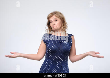 Verwirrte ältere Frau im blauen Kleid zuckt mit den Schultern, als keine Antwort wissen, Stockfoto