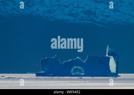 Eine absurde Eisskulptur fängt den schwindenden Licht und ist gegen die Verdunkelung Felswand in Ø Fjord, Grönland Stockfoto
