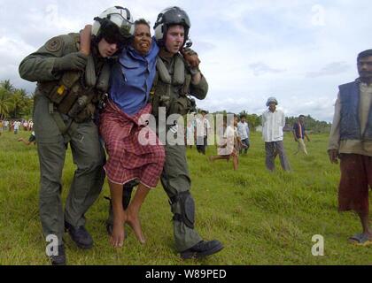 Zwei U.S. Navy aircrewmen vom Hubschrauber Anti-Submarine Squadron 2 tragen eine verletzte indonesische Frau einen Hubschrauber, um sie zu einer medizinischen Einrichtung, wo sie Aufmerksamkeit auf Jan. 3, 2005 erhalten zu transportieren. Die USS Abraham Lincoln Carrier Strike Group ist im indischen Ozean vor der Küste von Indonesien und Thailand im Rahmen der Operation Unified Hilfe. Stockfoto