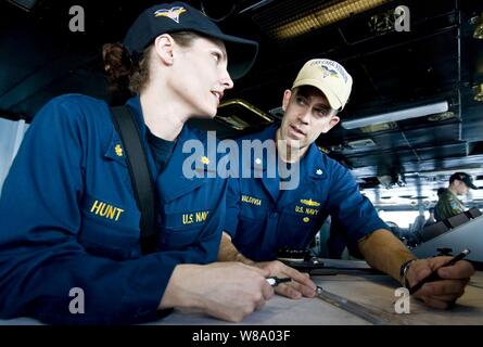 Cmdr. Christopher Valdivia, Hilfskräfte Offizier an Bord der Flugzeugträger USS Carl Vinson (CVN 70), erklärt, wie man plot Koordinaten des Schiffes Training Officer Lt.Cmdr. Amy Jagd auf der Brücke unterwegs in das Arabische Meer am 12. April 2011. Die Carl Vinson und Carrier Air Wing 17 leitend sind Maritime Security Operations und Unterstützung aus der Luft Missionen in den USA 5 Flotte Verantwortungsbereich. Stockfoto