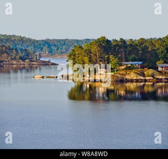 Cottages, Stuga, und Boote entlang der malerischen Inseln der Stockholmer Schären an der schwedischen Küste. Hohe Aussicht von der Ostsee Kreuzfahrtschiff Stockfoto