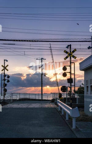 Anime stil Sonnenuntergang am Japanischen Bahnübergang in Matsuyama, Ehime Prefecture, Japan mit Blick auf das Meer und die Berge im Hintergrund Stockfoto