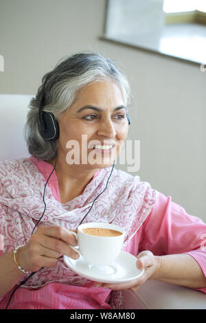 Ältere Frau Musik über Kopfhörer hören und trinken Tee Stockfoto