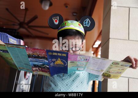 Ein Junge tragen Mickey Mouse headwear liest einen Tour Guide in der Shanghai Disneyland an der Shanghai Disney Resort in Pudong, Shanghai, China, 16 J Stockfoto