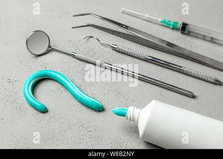 Zahnarzt Werkzeuge und Zahnpasta in der Form eines Fragezeichens. Spiegel, Haken, Pinzette und Spritze tools. Konzept, wie zu einem Zahnarzt wählen. Stockfoto
