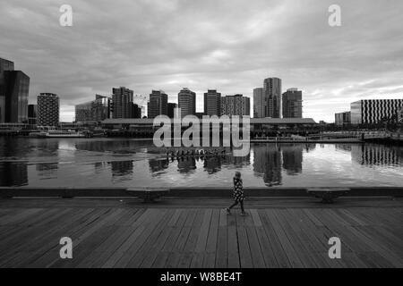 Teenager zu Fuß entlang der Pier in Docklands, während Sie paddeln Kajakfahrer mit Hochhäusern im Hintergrund. Melbourne, Australien Stockfoto