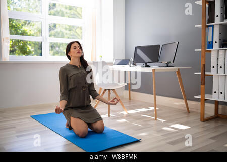 Entspannt junge Frau sitzt im Lotussitz auf Blau Trainingsmatte Stockfoto
