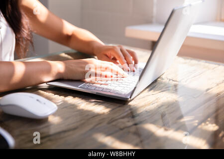 In der Nähe von Hand eintippen einer Person auf Laptop Tastatur auf dem Schreibtisch am Arbeitsplatz Stockfoto
