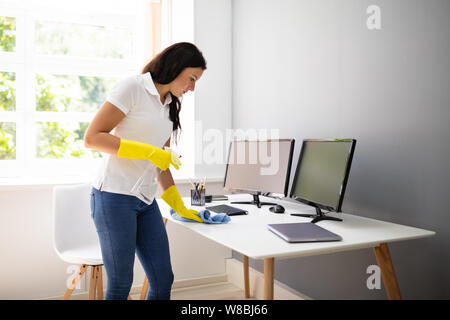 Seitenansicht der weiblichen Hausmeister Reinigung Schreibtisch mit Blau serviette im Büro Stockfoto