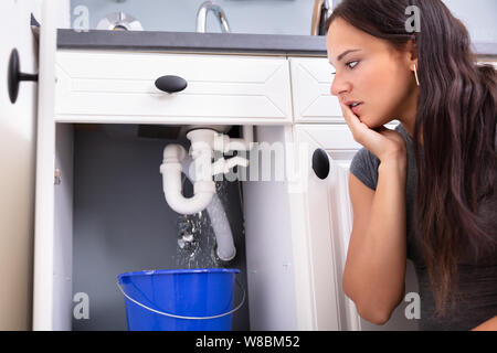 Junge Frau sammeln Leck Wasser im Eimer in der Küche Stockfoto