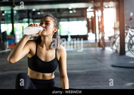 Sportlich schöne Frau Training entspannen und Wasser trinken mit Trainingsgeräten verschwommenen Hintergrund, Gesundes Leben und Gym Übung Ausrüstungen und Sport Stockfoto