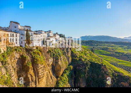 Ronda, Spanien: Landschaft der weißen Häuser am grünen Rand der steilen Klippen mit Bergen im Hintergrund. Stockfoto