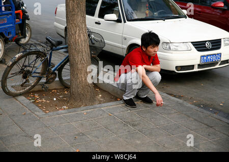 --FILE - Ein chinesischer Mann raucht eine Zigarette, als Er hockt auf einer Straße in Peking, China, 30. Juli 2014. China ist einer der größten Verbraucher von Tabak Stockfoto