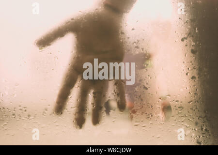 Menschliche Hand gedrückt gegen ein Fenster mit Tropfen Regen. Hand berühren Klarglas mit Wassertropfen. Natürliche Muster von Regentropfen von isolierten Stockfoto