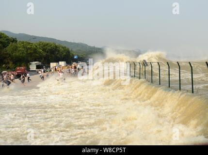 Besucher und Anwohner wie Wellen aus einem Tidal Bore Schwankung hinter einer Barriere am Ufer des Qiantang Fluss in Hangzhou City, East China Zhejian Stockfoto