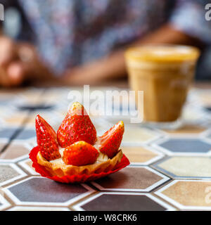 Ein Glas Kaffee Latte und Erdbeerkuchen auf eine farbenfrohe Keramik Tisch in einem Cafe. Quadratisches Bild. Stockfoto