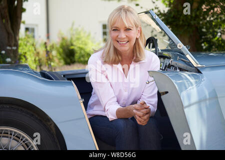 Portrait von Stolz, reife Frau sitzt in einem restaurierten klassischen Sportwagen im Freien zu Hause Stockfoto