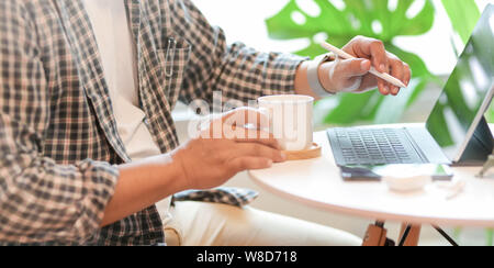 Junge männliche Freelancer arbeiten in komfortablen Arbeitsbereich beim Trinken einer Tasse Kaffee Stockfoto