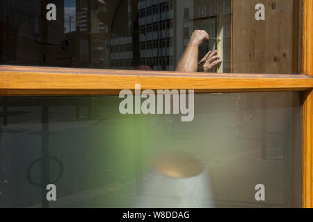 Gesehen, durch ein Fenster in eine Bar auf der Clerkenwell Road, eine Glatze workman strafft Schrauben auf einem Bilderrahmen, am 29. Juli 2019 in London, England Stockfoto