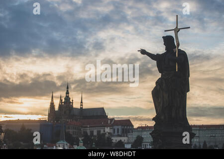 St. Johannes der Täufer Statue auf der Karlsbrücke in Prag mit St. Vitus Kathedrale im Hintergrund bei Sonnenuntergang. Stockfoto