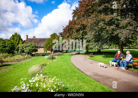 Northampton GROSSBRITANNIEN. 9. August 2019. Wetter. Nach schweren nächtlichen Regen Sonnenschein und blauen Wolken erscheinen am frühen Morgen in Abinton Park über dem Reetdachhaus in der oberen Park, mit ein paar Herren saß auf einer Bank in einem Chat. Credit: Keith J Smith./Alamy leben Nachrichten Stockfoto