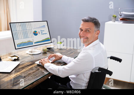 Behinderten Geschäftsmann sitzt im Rollstuhl und Computer im Büro Stockfoto